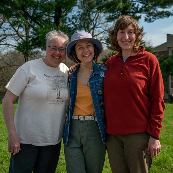 Three smiling people standing together outside on a grassy area