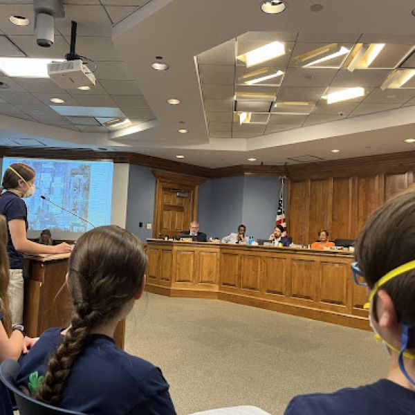 Student stands at a podium in a local government meeting setting