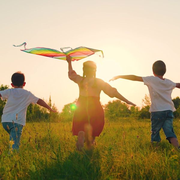 Three children running outside, one has a kite.